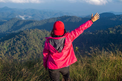 Rear view of carefree woman standing on field against sky