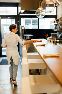 Female chef putting napkins on bar counter in open kitchen restaurant