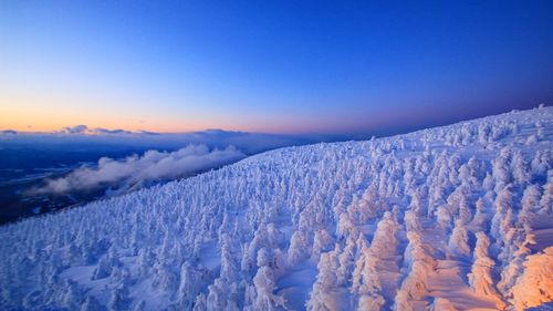 Scenic view of snow covered mountains against blue sky during sunset