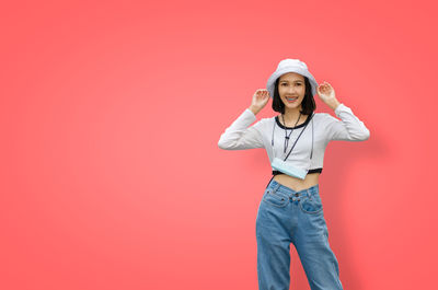 Portrait of young woman standing against pink background