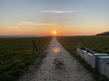 Walkway amidst field against sky during sunset