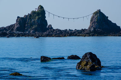 Wedded rock formation in sea against clear sky with shinto torii gate and shimenawa rope  