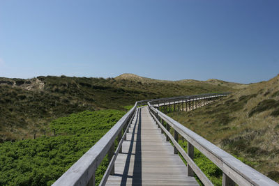 Footbridge leading towards mountains against clear blue sky