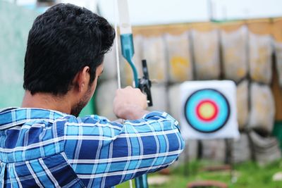 Rear view of man aiming at target with bow and arrow