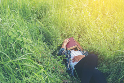 Man covering face with book while lying on grassy field