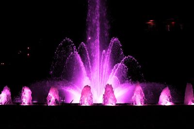 Illuminated firework display over fountain at night