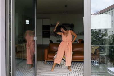 Cheerful woman dancing in living room seen through doorway