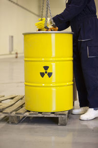 Low section of worker standing by yellow barrel with caution sign in factory