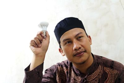 Portrait of young man holding camera against wall