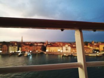 Close-up of railing by river against sky in city