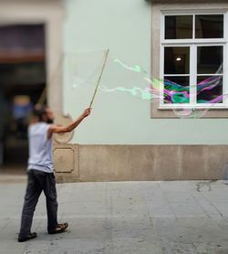 Full length of man holding bubbles while standing against wall