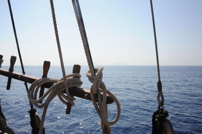 Ropes tied to wood of sailing ship in ocean against sky