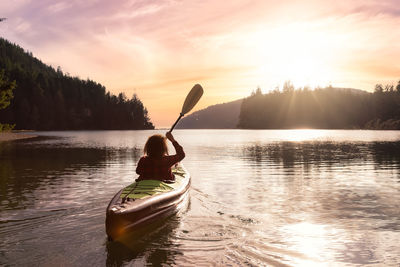 Man rowing boat in lake against sky during sunset