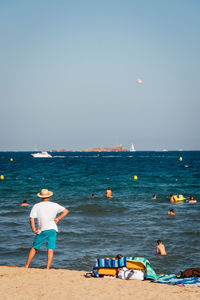 Rear view of man standing at beach against clear sky