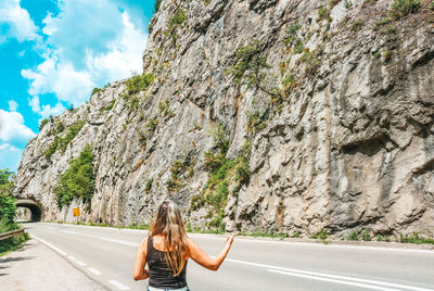 Rear view of woman standing by road against rock formation