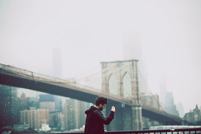 Man on bridge against sky in city