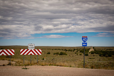 Road signs on landscape against cloudy sky