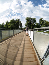 Man walking on footbridge against sky