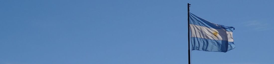 Low angle view of crane against blue sky argentinian flag