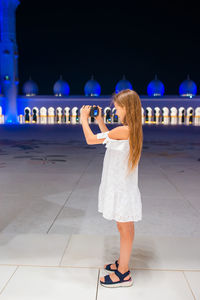 Full length of woman photographing with mobile phone standing at night