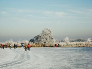 People ice skating on snowy landscape against sky