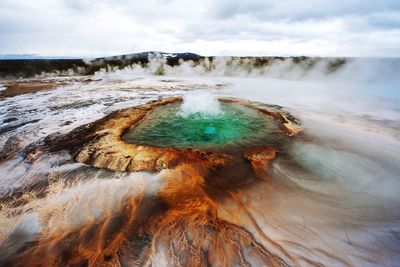 High angle view of geyser and field against cloudy sky