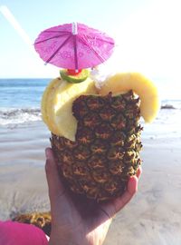 Cropped hand of woman holding pineapple at beach during sunny day