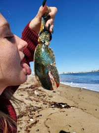 Close-up of woman holding crab at beach against clear sky