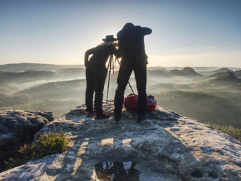 Couple of extreme creative artists work and talk on exposed rock with beautiful view into wild land