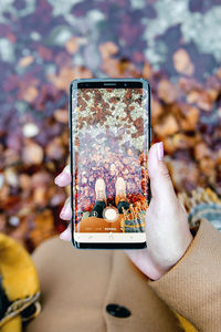 Low section of woman photographing while standing on field during autumn