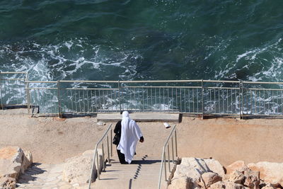 Rear view of woman walking on staircase by sea