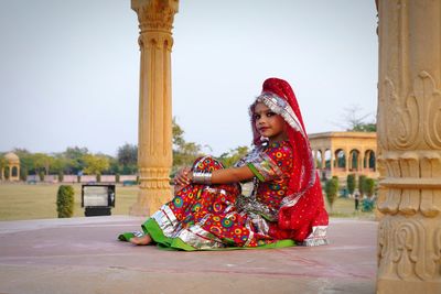 Side view of woman sitting against built structure