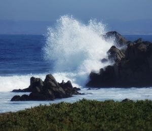 Waves breaking on rocks at shore against sky