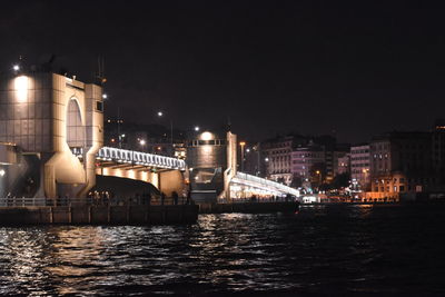 Illuminated bridge over river against sky in city at night