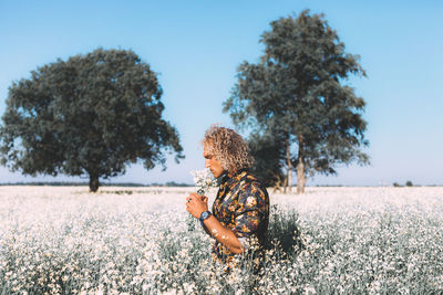 Man smelling flowers while standing against sky