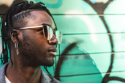 Close-up of young man wearing sunglasses against wall