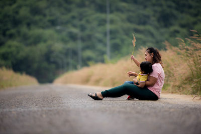 Side view of woman sitting with son on road against trees