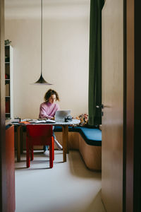 Full length view of young woman using laptop while doing homework at table