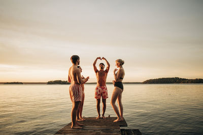 Friends looking at man gesturing while standing on jetty by lake during vacation