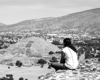 Rear view of woman sitting on mountain against sky