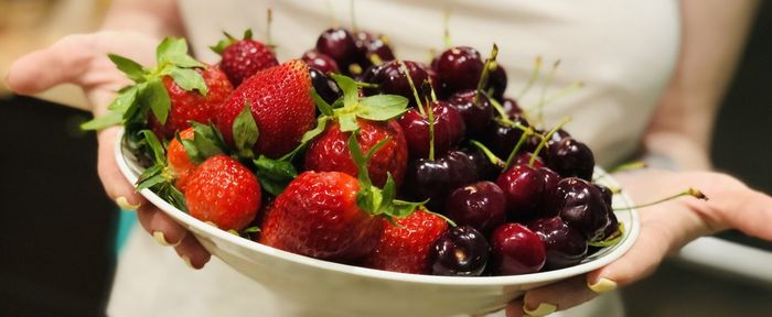 Midsection of person holding strawberries in bowl