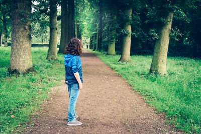 Side view of girl standing on footpath amidst field