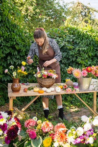 Cute florist girl collects a bouquet of autumn flowers in a basket on the table