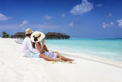 Couple relaxing at beach against sky