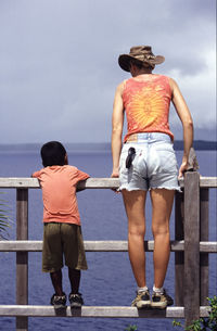 Rear view of woman and boy standing by sea against sky