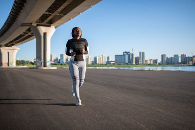 Ethnic sportswoman running under bridge