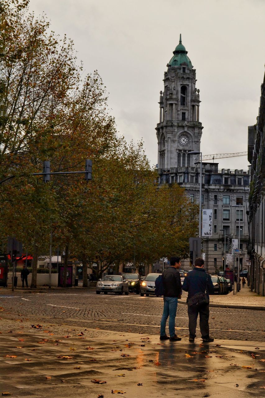 REAR VIEW OF PEOPLE WALKING ON STREET BY BUILDINGS IN CITY