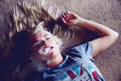 High angle view of young woman smoking while lying on carpet at home