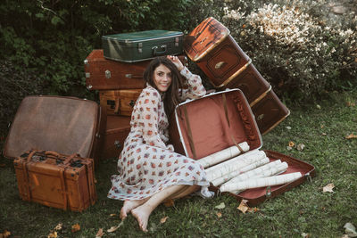 Full length of woman sitting by suitcases outdoors