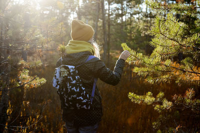 Rear view of woman standing by trees in forest